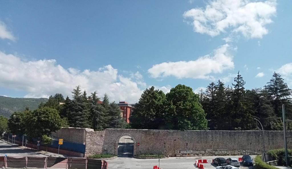 拉奎拉Hotel Porta Rivera Plesso Stazione的石墙,有隧道,树木和汽车