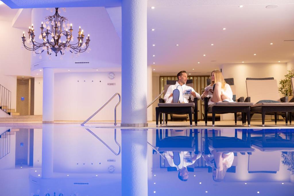 萨斯费Walliserhof Grand-Hotel & Spa Relais & Châteaux的两人坐在带游泳池的房间的椅子上