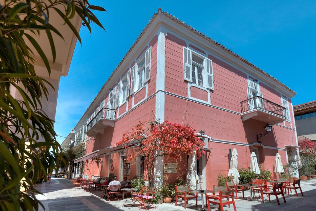 纳夫普利翁欧墨菲波利酒店的粉红色的建筑,前面设有桌椅