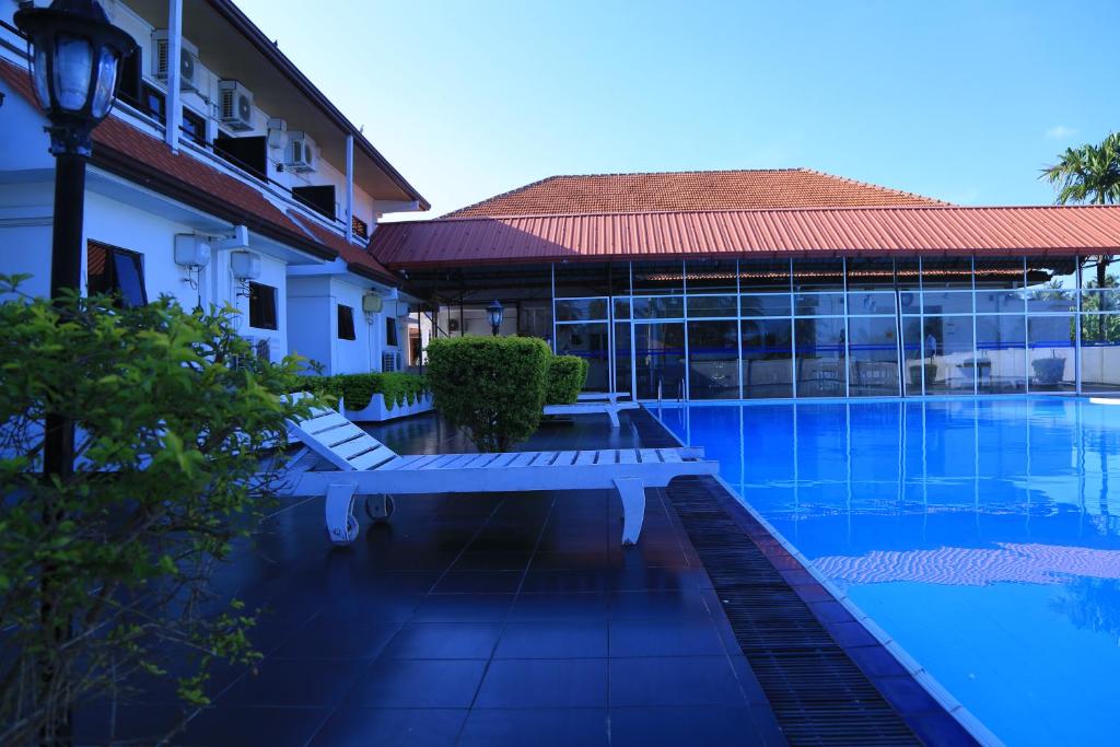 贾夫纳PJ Hotels Jaffna的一座带长椅的游泳池,位于大楼旁