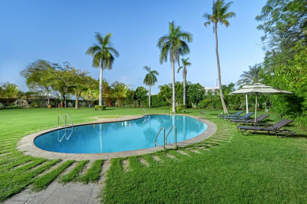 艾哈迈达巴德The Cama - A Sabarmati Riverfront Hotel的一个带椅子和遮阳伞的游泳池以及棕榈树