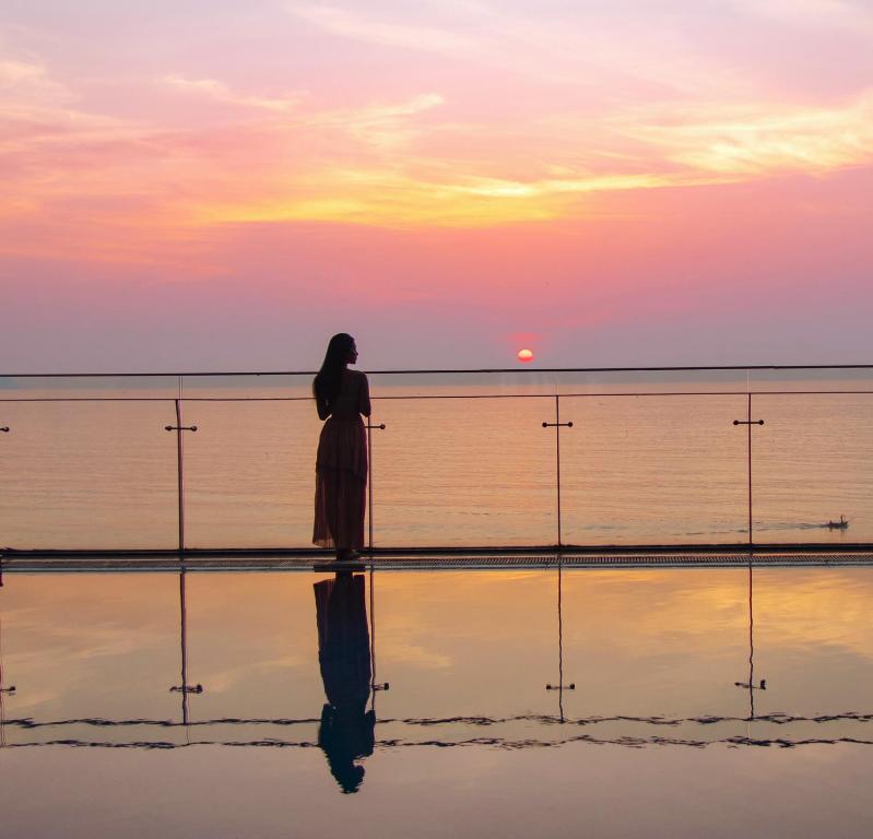 岘港Rosamia Da Nang Hotel的一位站在海滩上观看日落的女人