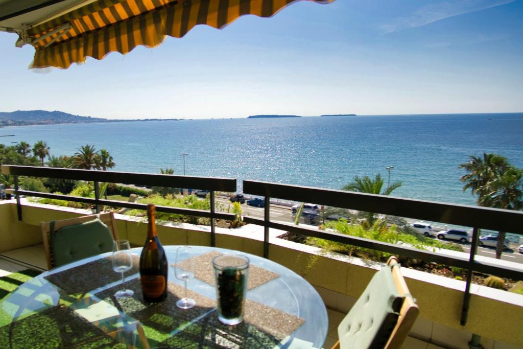 戛纳Ref EGEE - Palmes d'Or Properties的俯瞰大海的阳台的桌子和一瓶葡萄酒