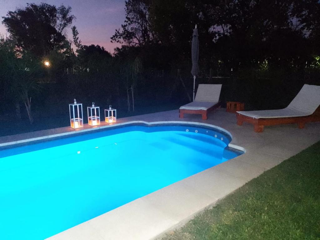 Villa Rosacasa con pileta climatizada, tiempo para descansar, Pilar的夜间游泳池,配有灯光和两把椅子