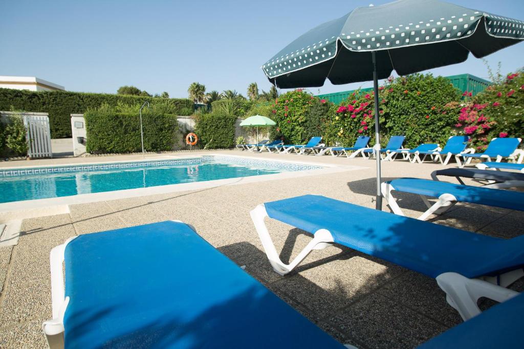博罗尼亚Apartamentos Bolonia Paraiso的一组椅子和一把遮阳伞,位于游泳池旁