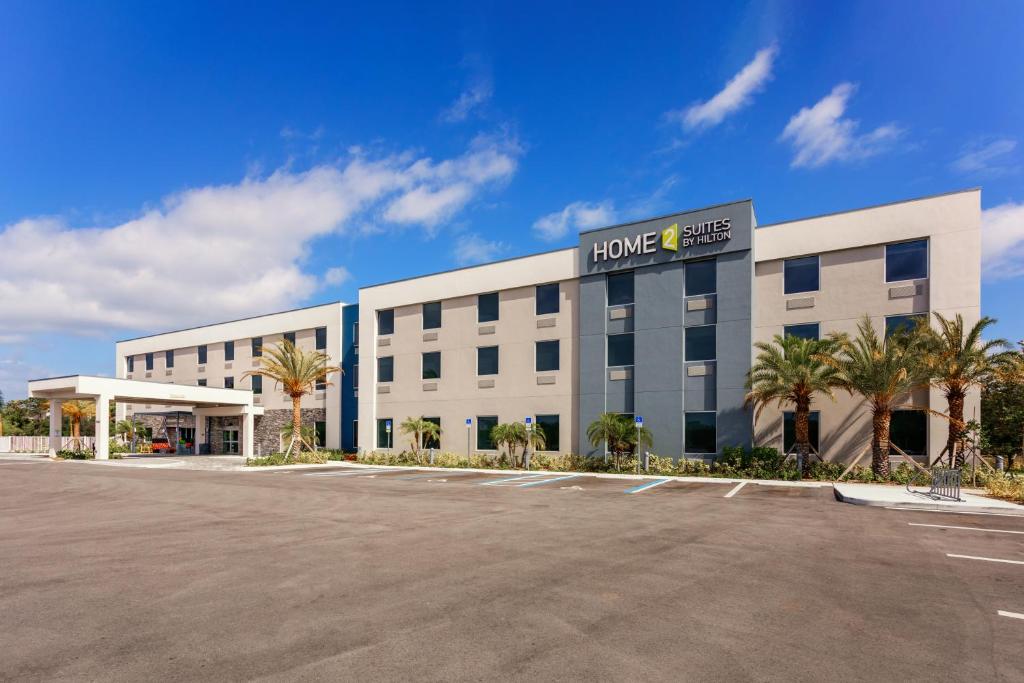 West Vero CorridorHome2 Suites By Hilton Vero Beach I-95的停车场内一座棕榈树成荫的大型白色建筑