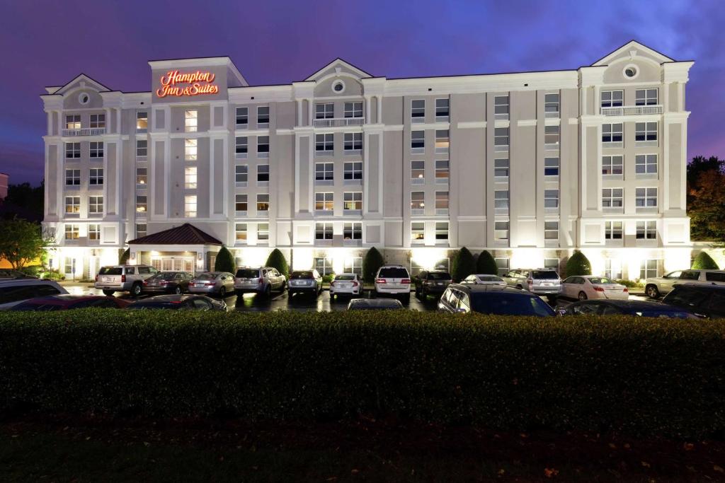 卡瑞Hampton Inn & Suites Raleigh/Cary I-40 (PNC Arena)的一座白色的大建筑,汽车停在停车场