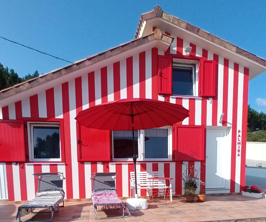 菲尼斯特雷Casiña Palmira的一座红色和白色的建筑,配有椅子和遮阳伞