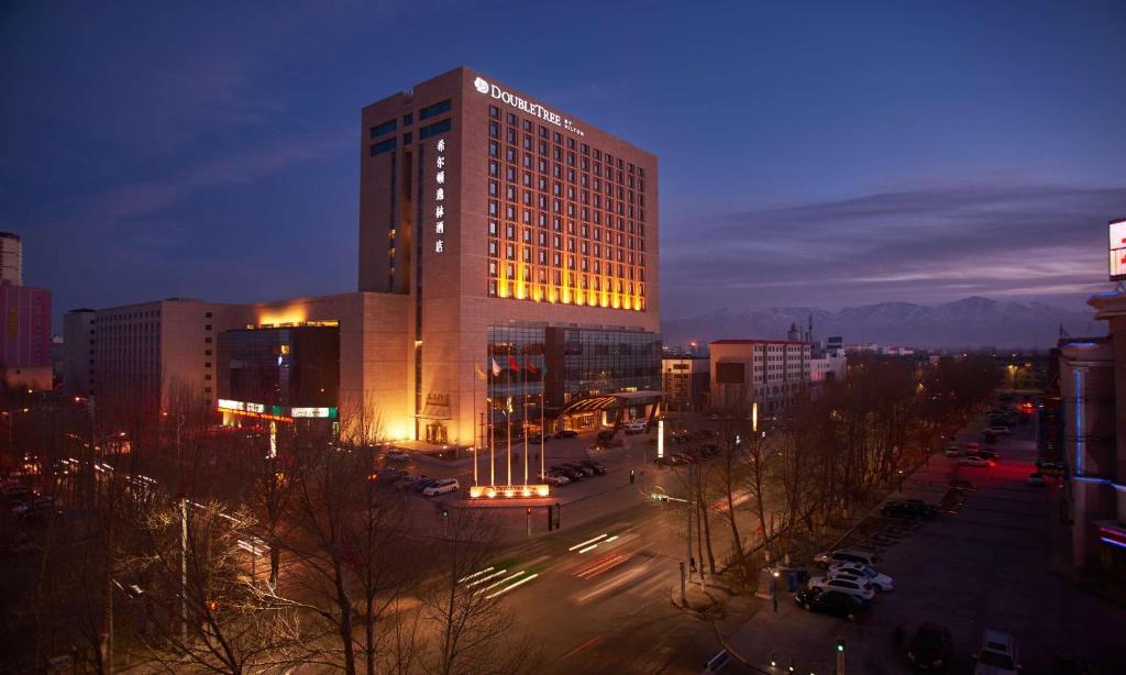 格尔木青海格尔木中浩希尔顿逸林酒店的一座高大的建筑,晚上在城市里亮着灯