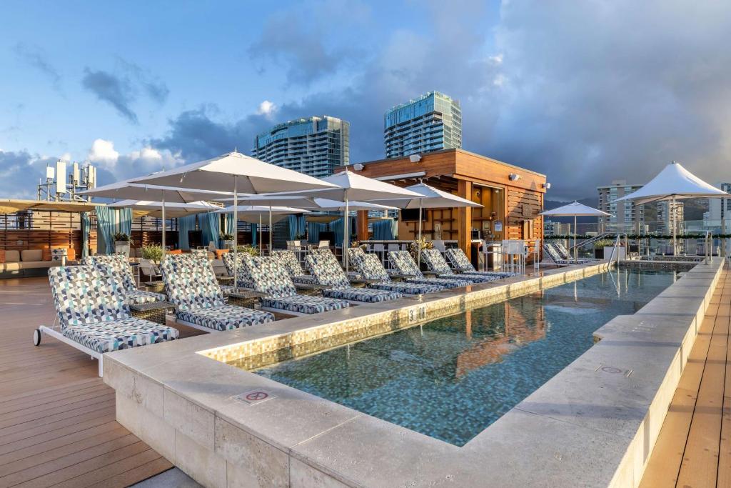 檀香山Hilton Grand Vacations Club Hokulani Waikiki Honolulu的大楼内一个带椅子和遮阳伞的游泳池