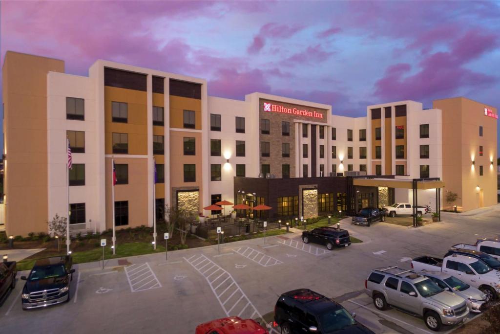 韦科Hilton Garden Inn Waco的停车场内有车辆的旅馆
