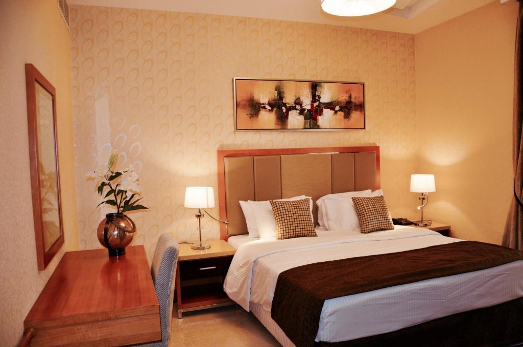 多哈阿什里酒店的一间卧室配有一张床和一张带两盏灯的桌子。