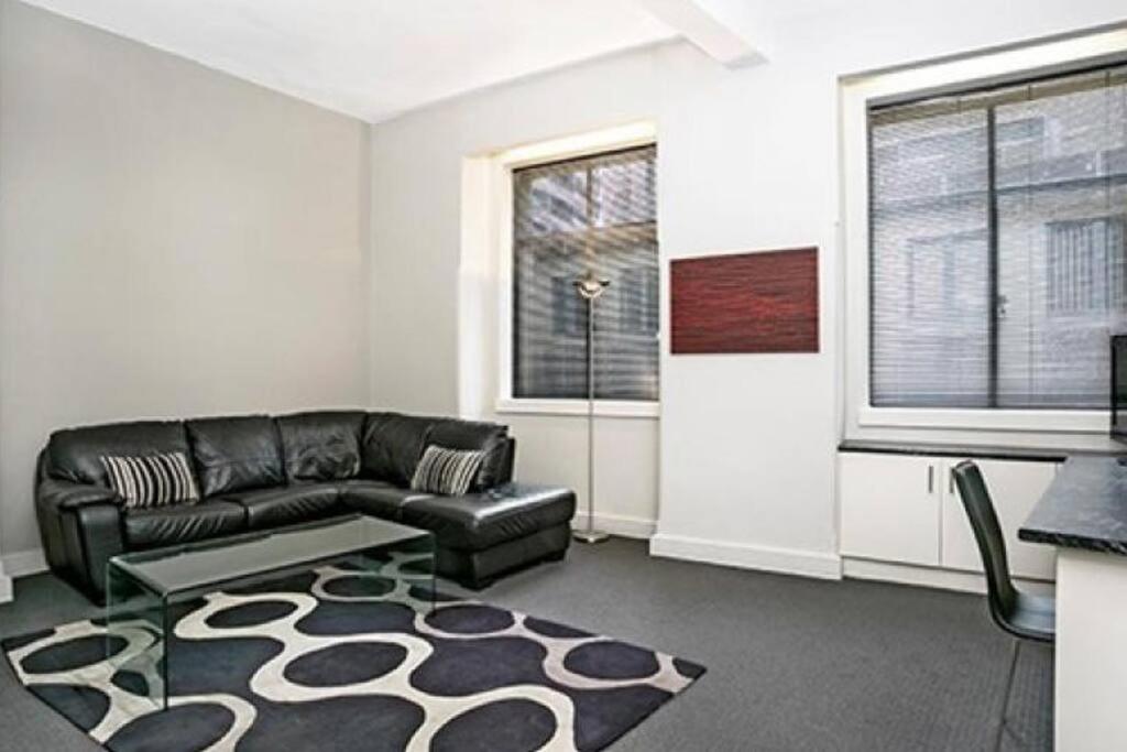 悉尼CLD01 - 1 bedroom unit - Bridge Street, Sydney CBD的客厅配有黑色皮沙发和地毯。