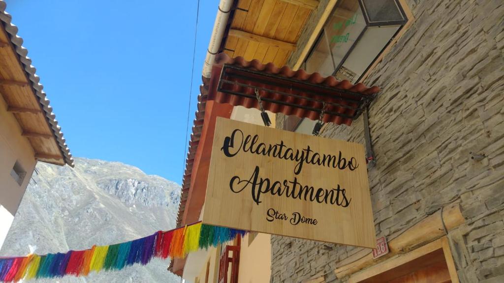 奥兰太坦波hostal ollantaytambo apartments的建筑物边的标志,带有彩虹横幅