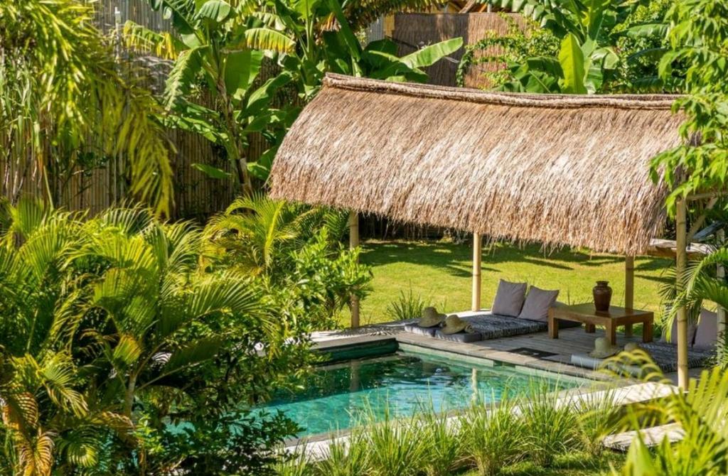 吉利阿尔Manusia Dunia Green Lodge的一个带游泳池和茅草屋顶的度假胜地