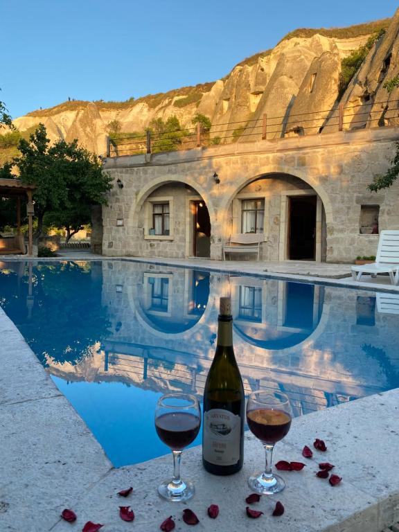 格雷梅Seven Rock Cave Hotel的游泳池旁的一瓶葡萄酒和两杯酒