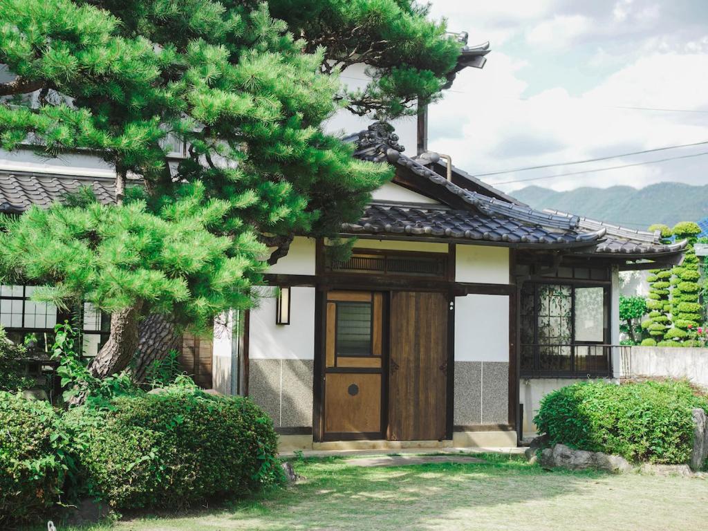 甲州古民家宿るうふ 蔦の家的一座日本房子前面有一棵树