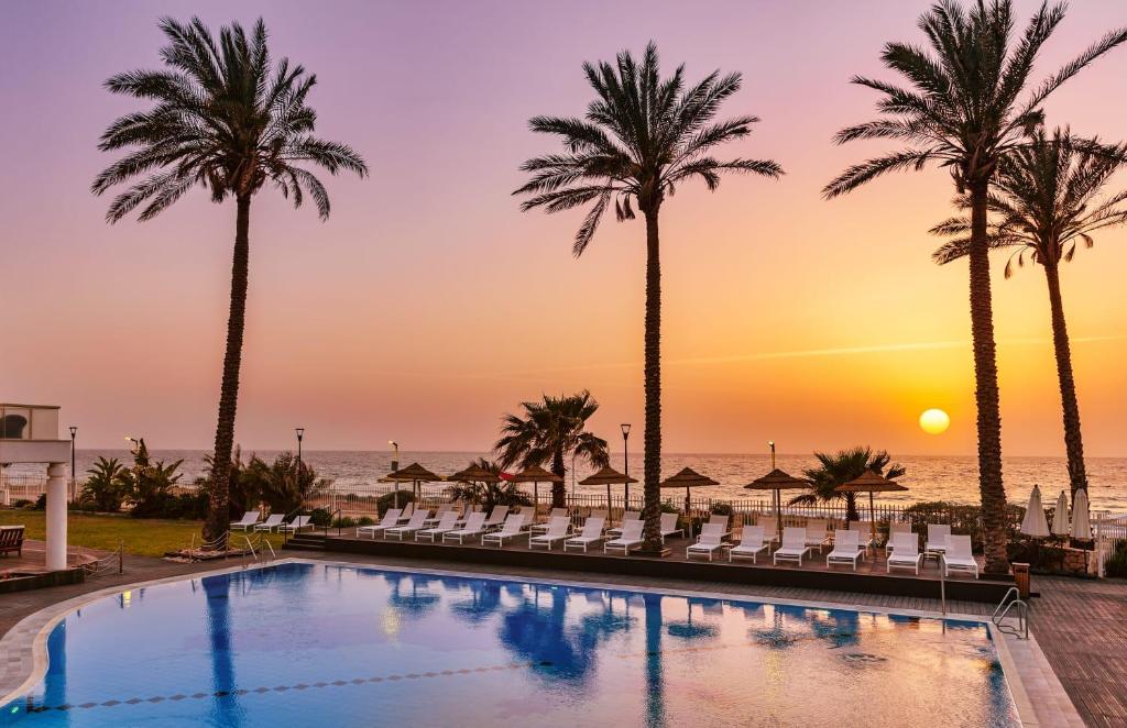 纳哈里亚Sea Life Nahariya BY Jacob Hotels的日落时分棕榈树和海洋的游泳池