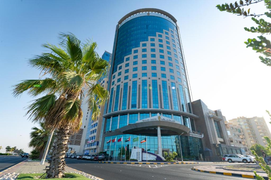 科威特Grand Hotel的一座高大的蓝色建筑,前面有一棵棕榈树