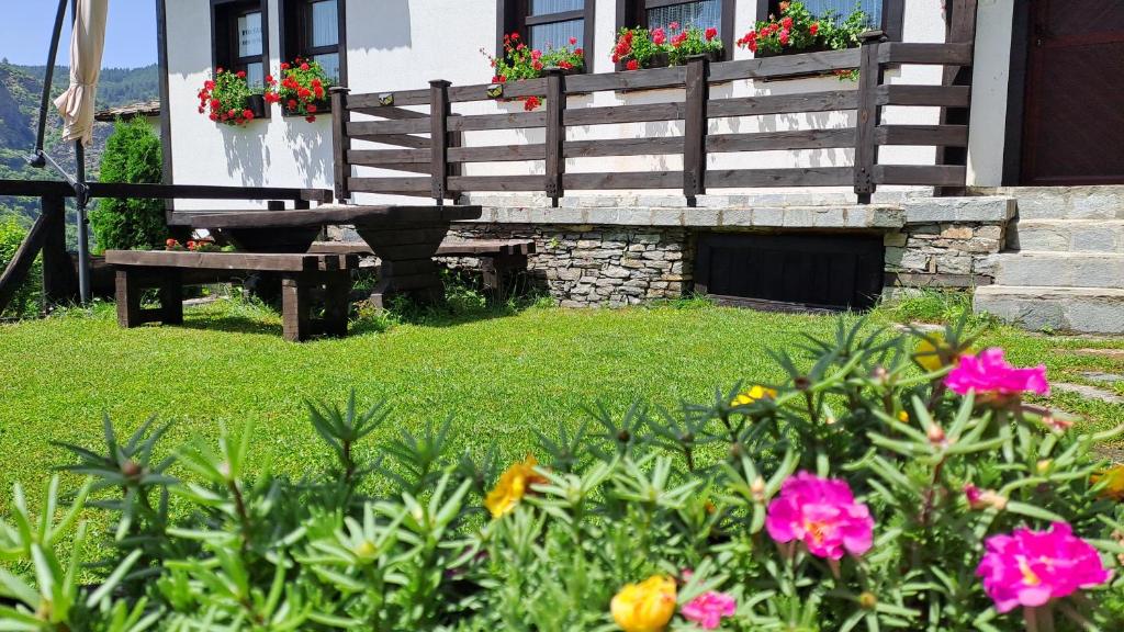 科瓦切维卡Къща за гости Далеч от морето的房屋前带长凳和鲜花的花园