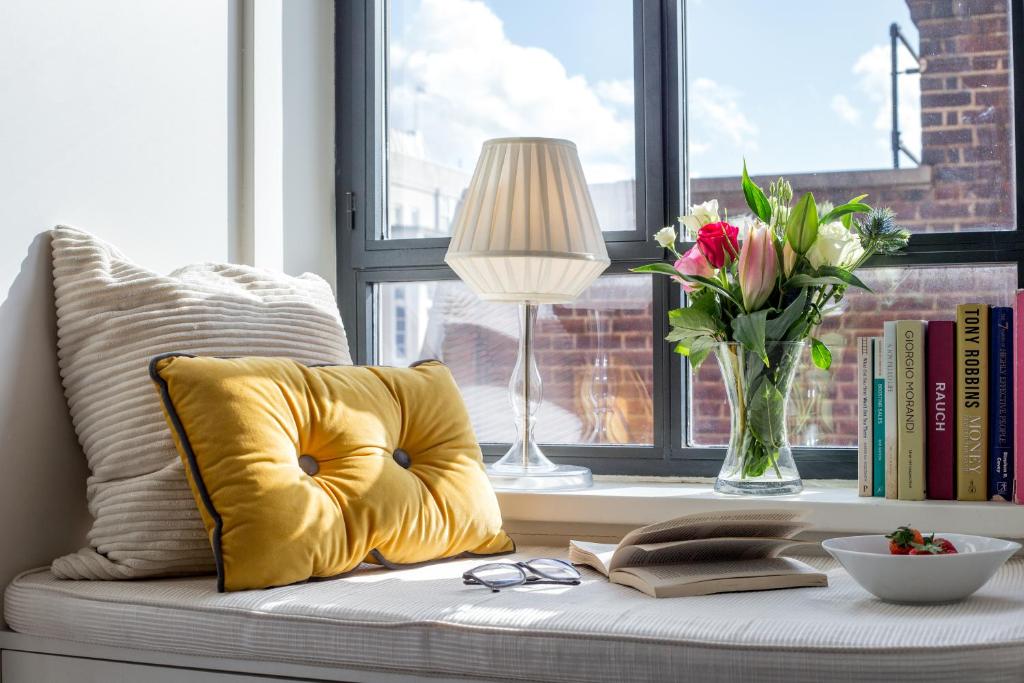 伦敦Chic 1BR Central London Retreat的黄色枕头坐在窗边座位上,花瓶