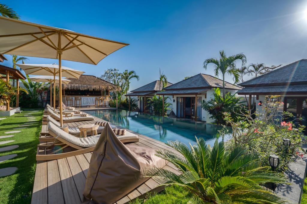 海神庙EHOA BALI Nyanyi Boutique Hotel的一张带椅子和遮阳伞的度假村游泳池的图片