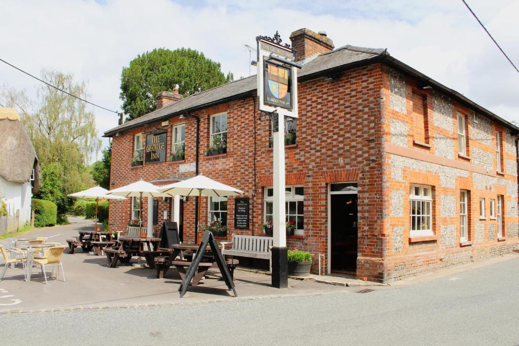 Saint Mary BourneThe George Inn St Mary Bourne的前面有桌子和遮阳伞的砖砌建筑