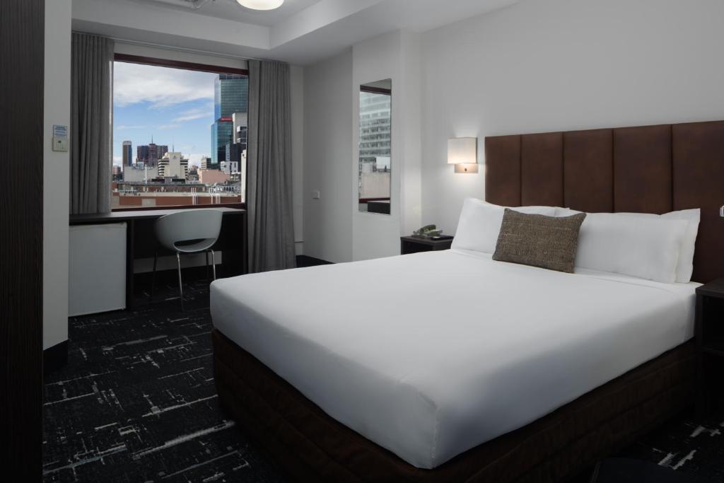 墨尔本墨尔本美居迎宾馆的配有一张床、一张书桌和一扇窗户的酒店客房