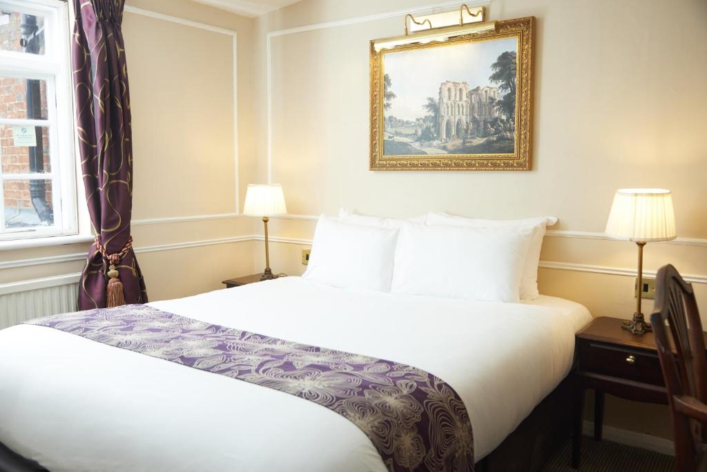 斯托尼斯特拉特福Cock Hotel by Greene King Inns的酒店客房设有一张床,墙上挂着一张照片