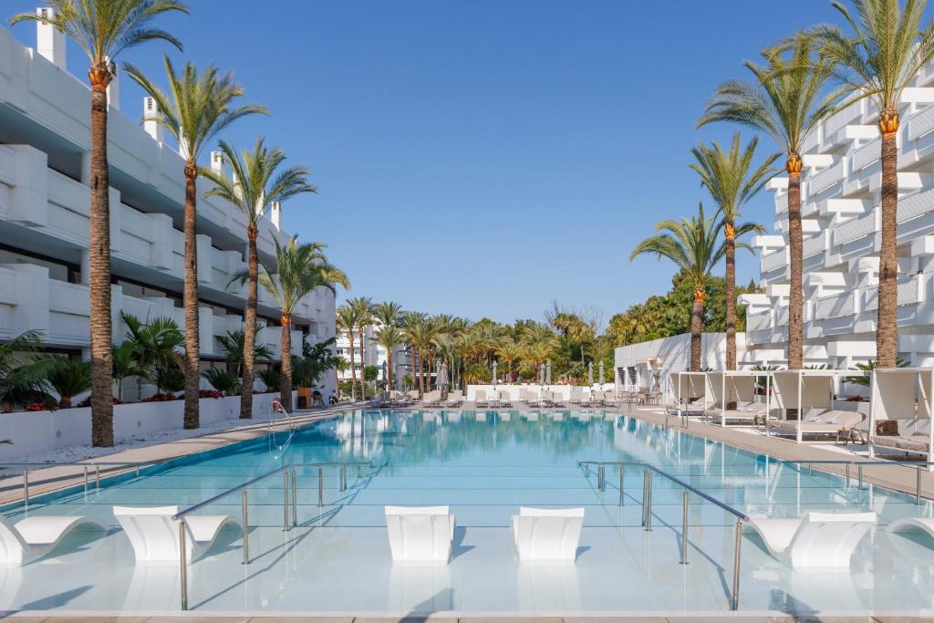 马贝拉Alanda Marbella Hotel的一座带椅子和棕榈树的游泳池,位于一座建筑前