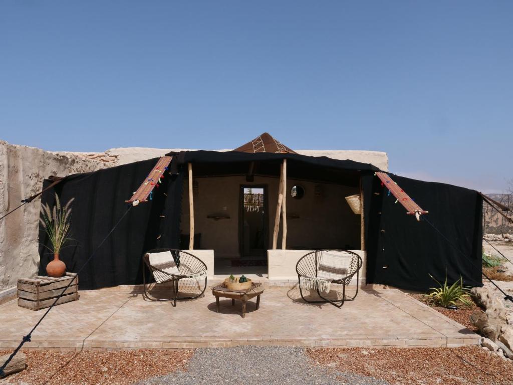 依索安Berber Beldi Camp的黑色帐篷前配有椅子和桌子