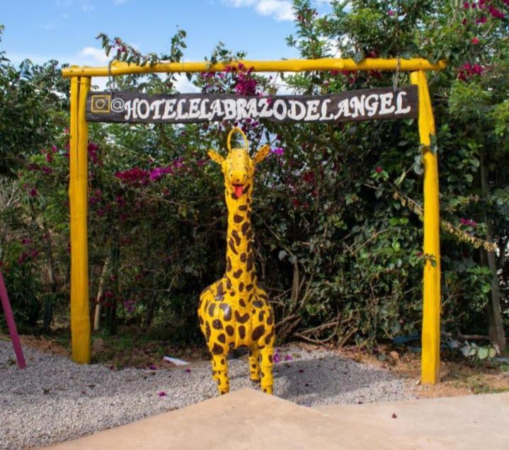AratocaHOTEL CAMPESTRE ABRAZO DEL ANGEL的长颈鹿雕像站在标志前