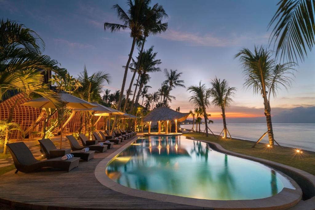珀尼达岛The Sankara Beach Resort - Nusa Penida的黄昏时分带躺椅和海洋的度假游泳池