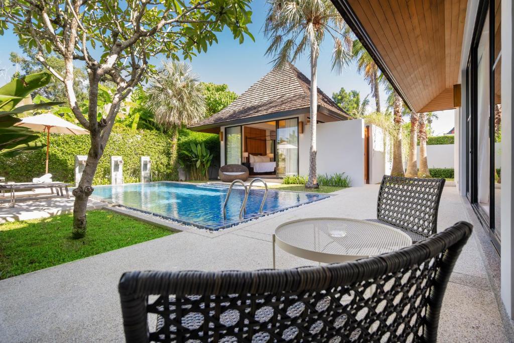 Ban Phru ChampaEscape Villas - Luxury Pool Villa at Anchan Villas的游泳池旁带桌椅的天井