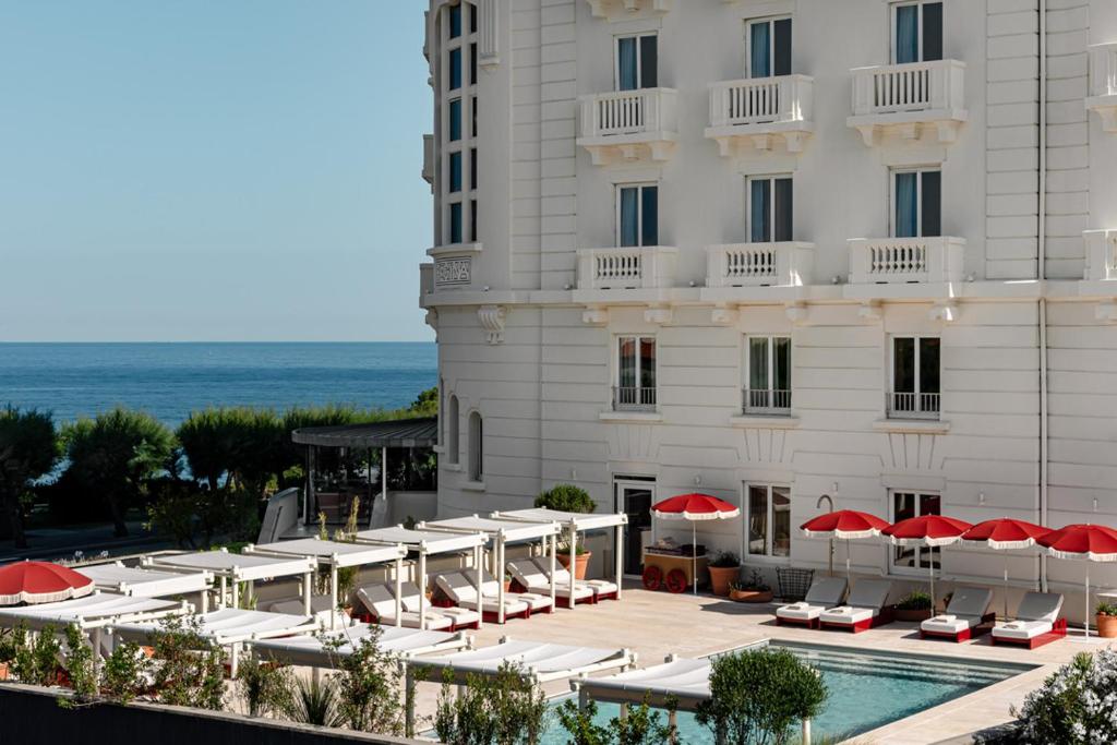 比亚里茨Regina Experimental Biarritz的一个带游泳池、椅子和遮阳伞的酒店