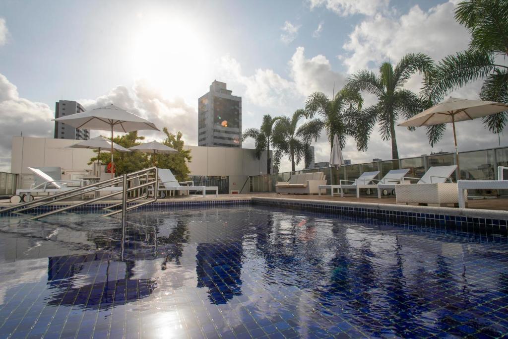 累西腓Bugan Recife Boa Viagem Hotel - by Atlantica的一座大楼内的游泳池,配有椅子和遮阳伞