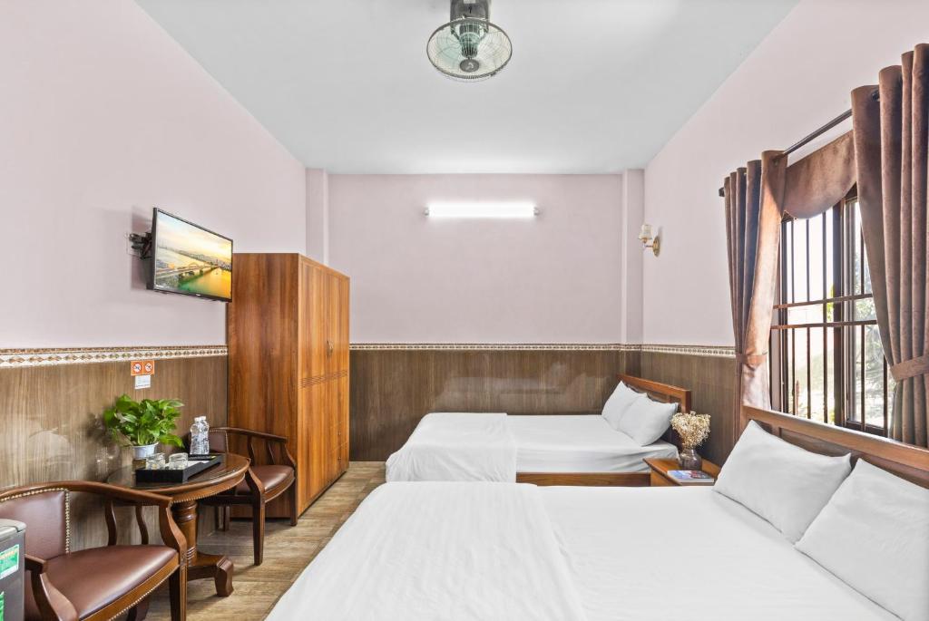岘港Mộc Nhiên Hotel Da Nang的酒店客房带两张床和一张桌子以及椅子。