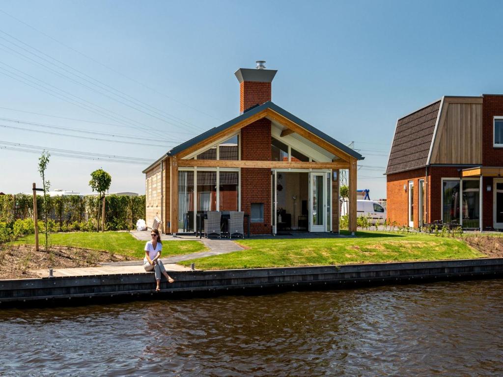 阿克伦Disabled house on the water, on a holiday park in Friesland的坐在房子前面的码头上的女人