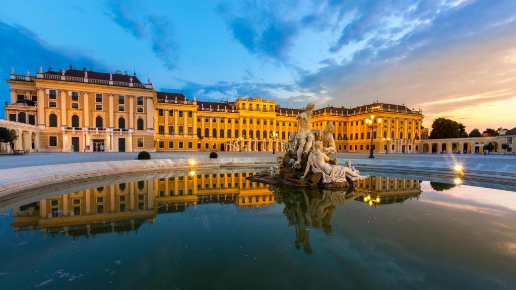 维也纳Schönbrunn Serenity Luxurious Ruby Apartment with Palace Views的一座黄色的大建筑,前面有一个喷泉