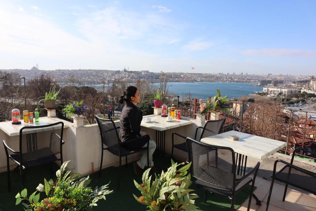 伊斯坦布尔Galata istanbul Hotel的坐在阳台上的桌子上的女人,俯瞰城市
