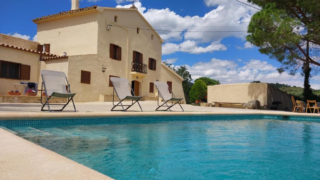 El Pla de ManlleuCasa Rural Cal Martí的两把椅子和一个位于房子前面的游泳池