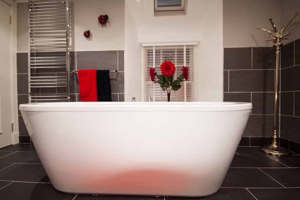 圣安德鲁斯亚格丽34号旅馆的浴室设有白色浴缸,装饰有红色的鲜花。
