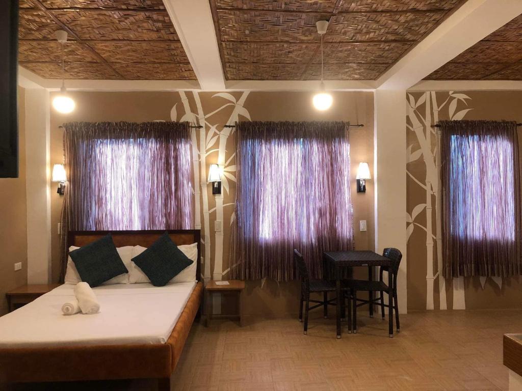 班塔延岛Anahaw Seaside Inn的一间卧室配有一张床、一张桌子和两个窗户