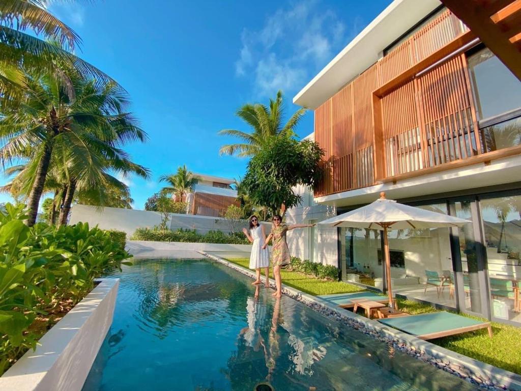 富国Phoenix Pool Villa Phu Quoc的两个人站在房子前面的游泳池边