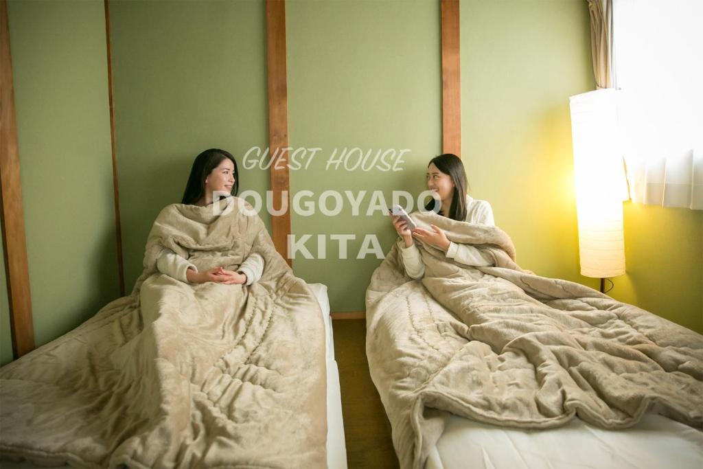 松山GUEST HOUSE DOUGOYADO KITA - Vacation STAY 14923的两名妇女坐在房间里的床里