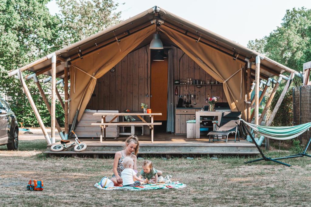 霍尔滕Glamping Holten luxe safaritent 2的一名妇女和两名儿童坐在帐篷前