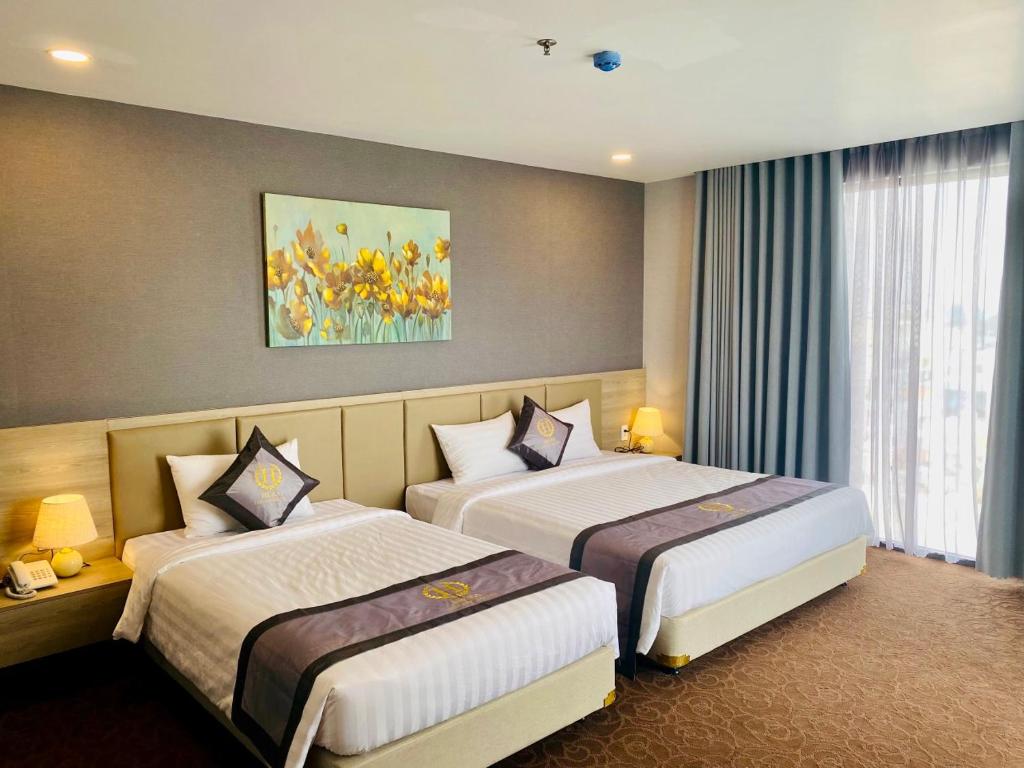 胡志明市Hera Luxury Hotel的酒店客房设有两张床,墙上挂有绘画作品