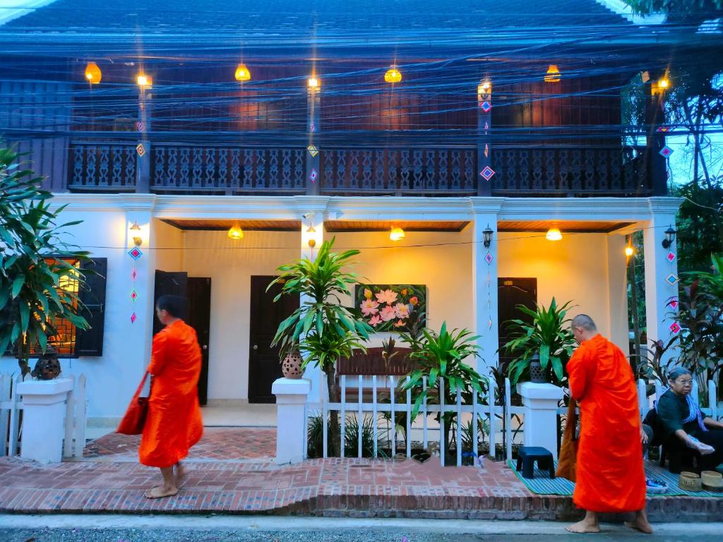 琅勃拉邦Lotus Corner - Vegan & Plant Based B&B的三位身着橙色长袍的僧侣站在房子前面
