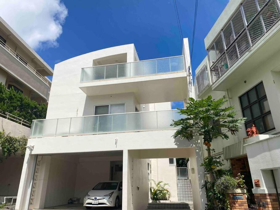 那霸Vacation Rental Kally Naha Okinawa的带阳台和汽车的白色房屋