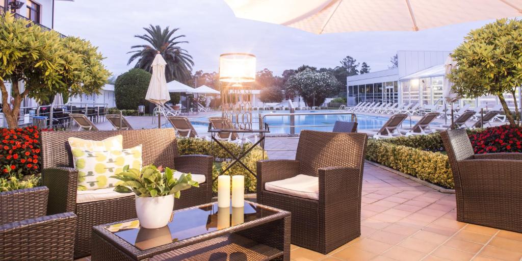 桑亨霍Nuevo Astur Spa的一个带柳条椅和桌子的庭院和一个游泳池